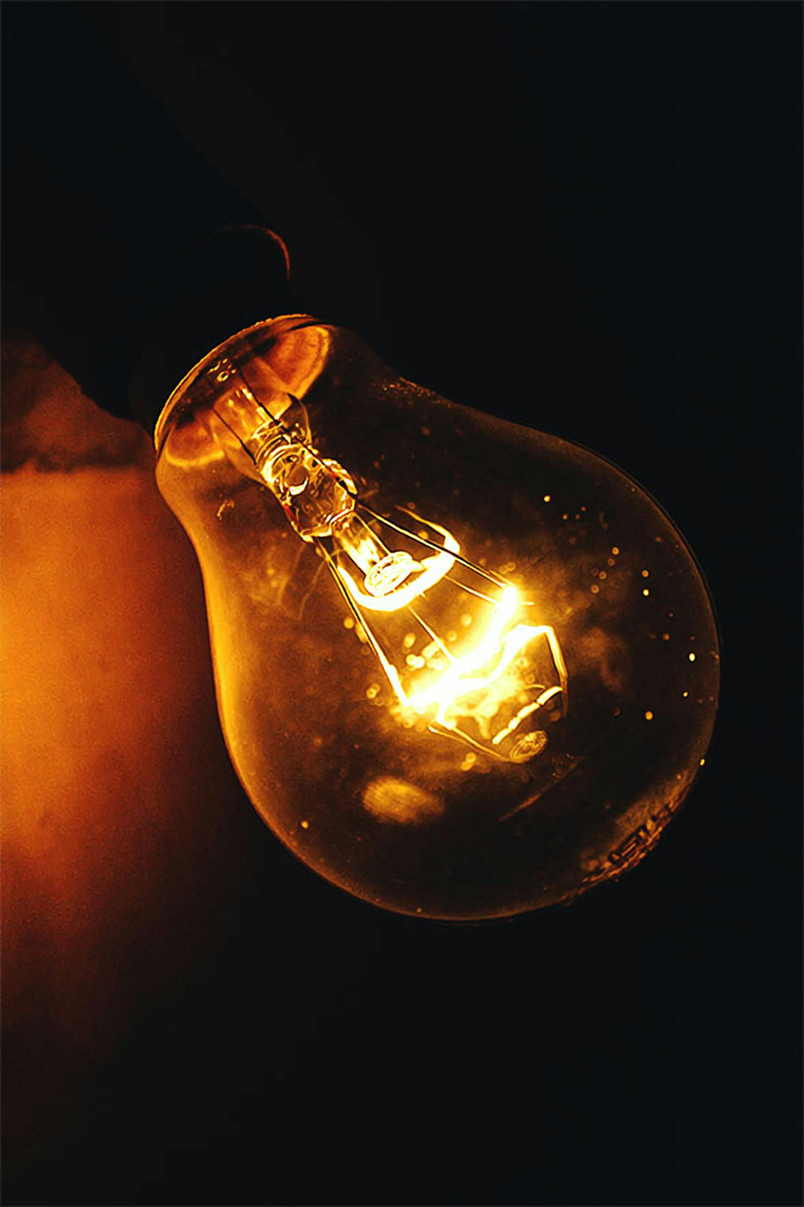Close-up of a glowing incandescent light bulb illuminating a dark space.
